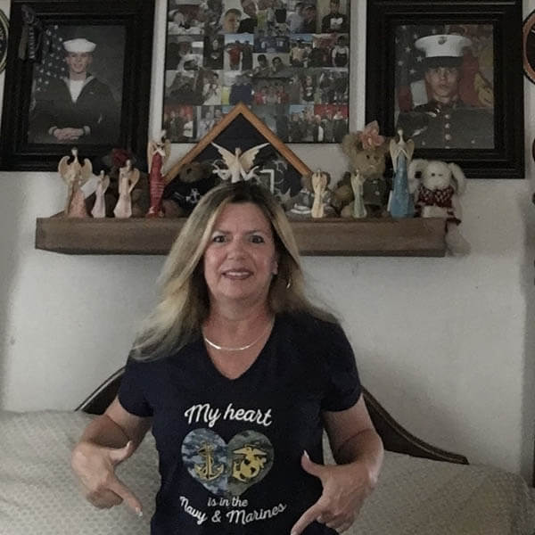 Military Mom of sailor and marine proudly show off her shirts in front of their soldier's photos